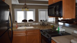 A kitchen with wooden cabinets, a black refrigerator, a microwave, a stove, and a chandelier.