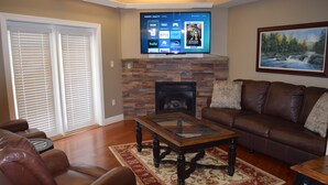 A living room with a fireplace, leather sofa, and a flat-screen TV mounted above it.