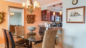 A dining area with a glass table, woven chairs, and a chandelier. - 🌅 Islander #303 – Luxury Living with Breathtaking Sunrise Views! 🌊✨ (Destin)
