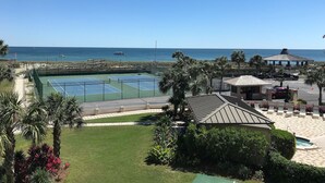 A tennis court with a view of the ocean, palm trees, and a gazebo. - 🌅 Islander #303 – Luxury Living with Breathtaking Sunrise Views! 🌊✨ (Destin)