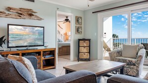 A living room with a TV, sofa, coffee table, and a view of the ocean. - 🌅 Islander #303 – Luxury Living with Breathtaking Sunrise Views! 🌊✨ (Destin)