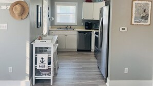 Una cucina compatta con mobili bianchi, un frigorifero in acciaio inossidabile e una piccola isola con lavello.
