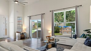 Ett rymligt vardagsrum med ett stort fönster, en takfläkt och utsikt över ett bostadsområde.