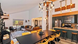 A modern kitchen with stainless steel appliances, a dining area with a black table and yellow chairs, and a stone accent wall. - Rise and Shine by Destination Big Bear : Pool Table! Shuffleboard! Walk to the Lake! Near Snow Summit! Internet! (Big bear lake)