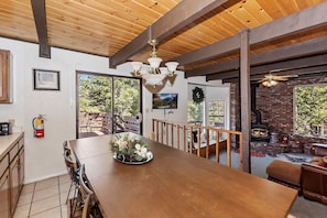 Enjoy meals in this dining area with a long table for four, high ceiling, and large windows offering garden views.