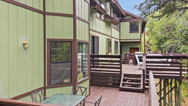 Una terraza de madera con una mesa y sillas, una valla de madera, y un edificio con varias ventanas.