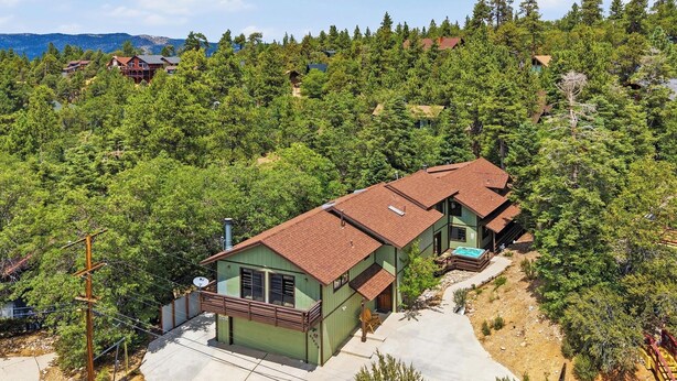 A two-story house with a green exterior and a brown roof, surrounded by dense forest. - Movie Theater! Pool Table! HOT TUB! Mtn Views! Multiple Decks! (Big Bear Lake)