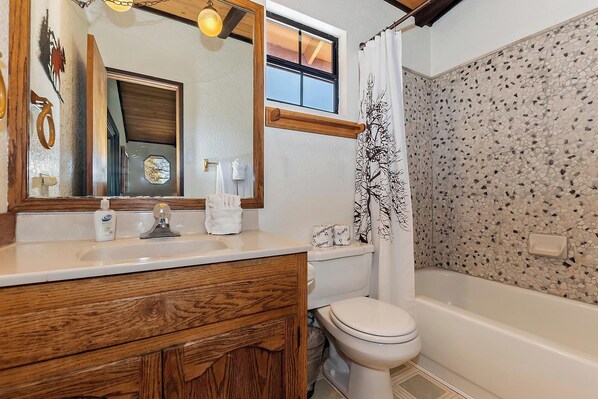 A bathroom with a wooden vanity, a toilet, a bathtub, and a shower curtain with a tree design.