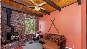 A cozy living room with a brick fireplace, leather sofa, and a ceiling fan. - Movie Theater! Pool Table! HOT TUB! Mtn Views! Multiple Decks! (Big Bear Lake)