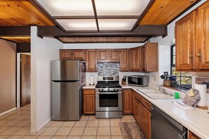 Una cocina con armarios de madera, electrodomésticos de acero inoxidable y piso de baldosas.