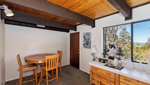 A room with a wooden ceiling, a round table with chairs, a window with a view of trees, and a cabinet with decorative items. - Movie Theater! Pool Table! HOT TUB! Mtn Views! Multiple Decks! (Big Bear Lake)