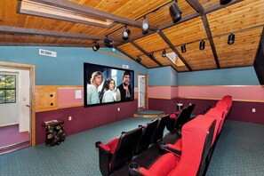 Ein Theater mit Holzbalkendecke, einer großen Leinwand, roten Sitzen und einer Tür mit dem Warnhinweis 'CAUTION'.