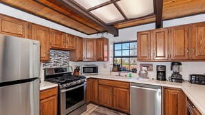 A kitchen with wooden cabinets, stainless steel appliances, and a large window. - Movie Theater! Pool Table! HOT TUB! Mtn Views! Multiple Decks! (Big Bear Lake)