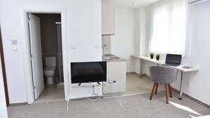 Un espacio habitable moderno y funcional con kitchenette, comedor y pequeño escritorio.