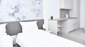 Una habitación de hotel moderna con una cama, una kitchenette pequeña y una pared de mármol.