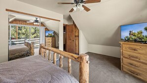 A bedroom with a bed, wooden dresser, TV, ceiling fan, and a view of the outdoors.