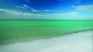 Una playa con agua turquesa cristalina y una orilla de arena blanca bajo un cielo azul.
