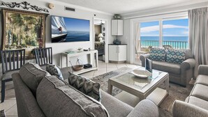 Ein geräumiges Wohnzimmer mit großem Fernseher, bequemen Sitzgelegenheiten, einem Essbereich und einem Balkon mit Meerblick.