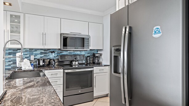 Una cocina moderna con armarios blancos, un refrigerador de acero inoxidable, un microondas, una estufa y una cafetera.