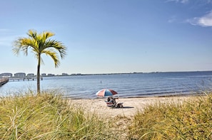 Eine Strandansicht mit einer Palme, einer Person unter einem Sonnenschirm und einer weiter entfernten Stadtansicht.