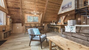 Ett rymligt rum i loftstil med högt tak, synliga träbjälkar, en matplats och en mysig sittgrupp med en soffa och en bänk.