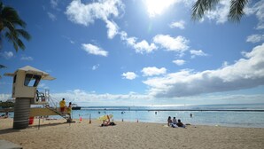 A beach with a lifeguard tower, palm trees, and people relaxing on the sand. - Renovated Private Kuhio Village 708A Studio - 2 min Walk 2 the Beach! (Honolulu)