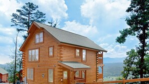 A log cabin with a porch, a small deck, and a scenic mountain view.