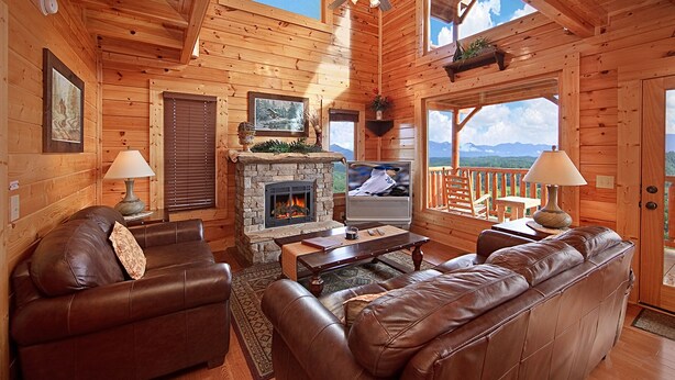 A cozy log cabin interior with a stone fireplace, leather sofas, and a television.