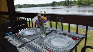 Een tafel voor twee, gedekt met borden, bestek en een bloevas, op een balkon met uitzicht over een meer.