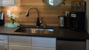 Een keuken met een houten plafond, een ronde wandklok, een koffiezetapparaat, en een bord met de tekst 'Het leven is beter aan het meer'.