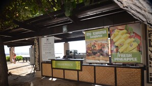 A beachside kiosk with a sign for 'Grass Shack Bistro' and menu options like 'Big Kahuna Sandwich' and 'Fresh Pineapple'.