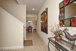 A hallway with a dining area in the background, a vase with flowers, and a decorative metal sculpture.