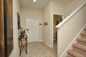 A hallway with a white door, a small table with a plant, a coat rack, and a staircase.