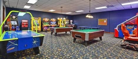 A room with pool tables, arcade games, and a patterned carpet.