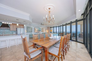 Uma sala de jantar espaçosa com uma grande mesa de madeira, várias cadeiras e um lustre.