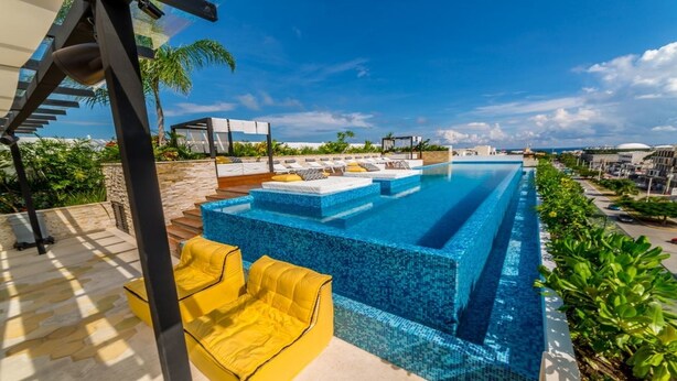 En modern infinitypool med fri utsikt över havet, omgiven av solstolar och en stenmur.