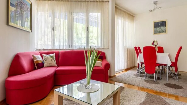 A living room with a red sofa, a glass coffee table, and a dining area with red chairs and a white table. - Three BR ✦ Fully equipped large apartment✦ City center and beach proximity ✦ (Split)