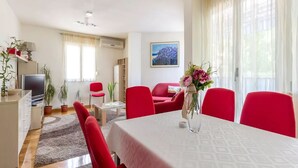 A modern living room with a dining area, red furniture, and a large window with sheer curtains. - Three BR ✦ Fully equipped large apartment✦ City center and beach proximity ✦ (Split)