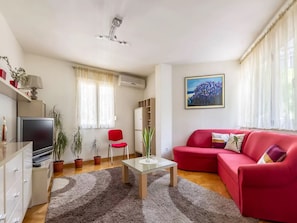 Un salon avec un canapé rouge, une table basse en verre, un téléviseur et un tableau accroché au mur.