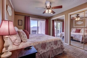 A bedroom with a bed, a nightstand, a lamp, a ceiling fan, and a large mirror.