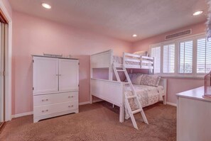 A bedroom with a bunk bed, a white wardrobe, and a window with blinds.