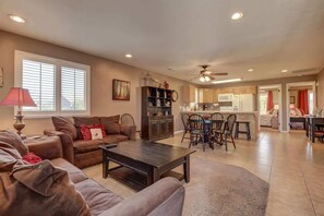 A spacious living room with a brown leather sofa, a coffee table, and a dining area with chairs and a kitchen in the background. - Las Palmas Resort #110 | All-Inclusive Amenities (Saint George)