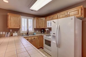 A kitchen with wooden cabinets, a white refrigerator, a stove, and a window with blinds. - Las Palmas Resort #110 | All-Inclusive Amenities (Saint George)