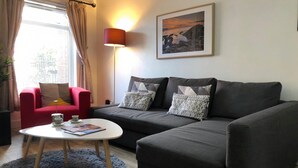 Un salon avec un canapé gris, un fauteuil rouge et une table basse blanche.