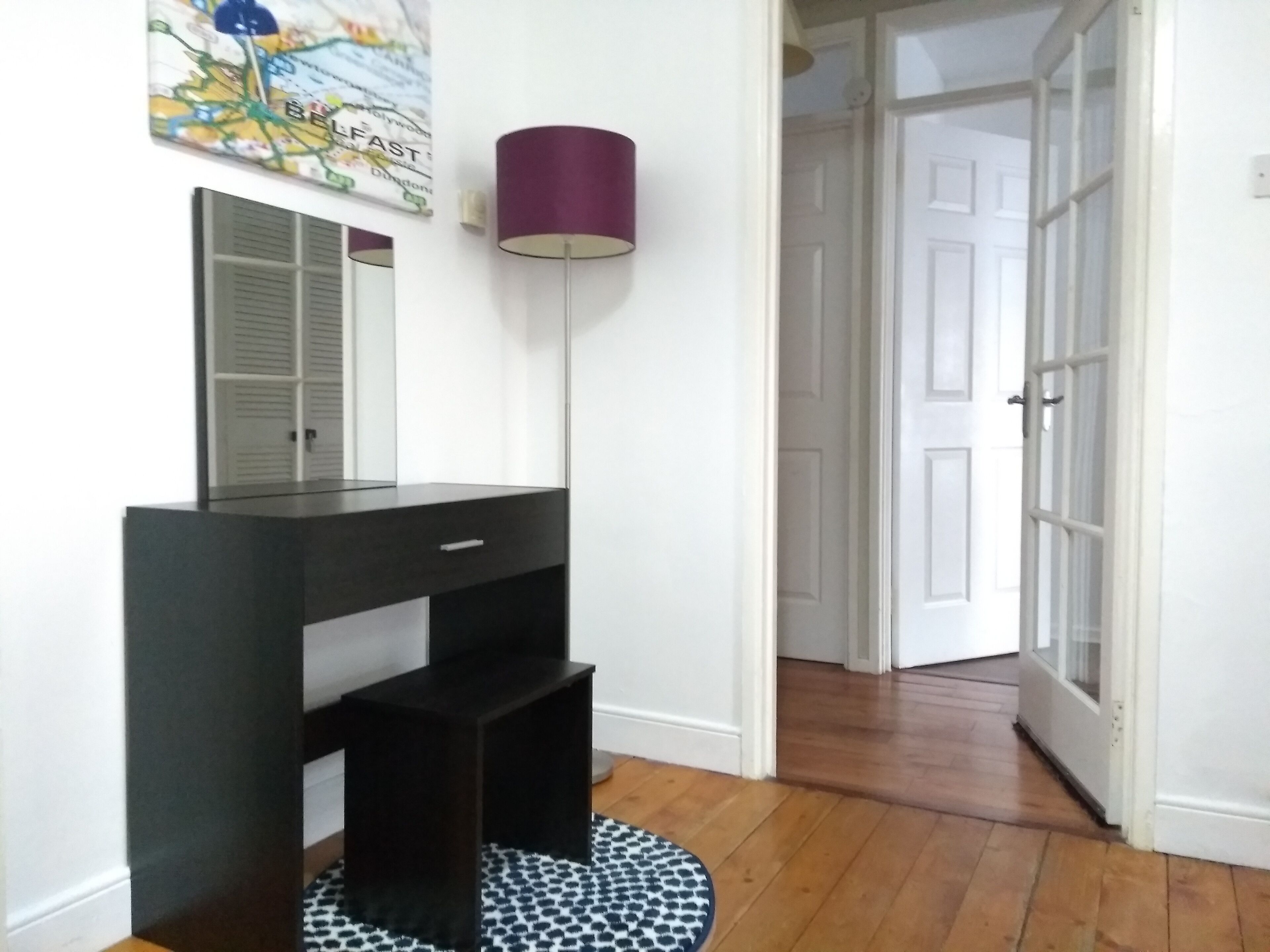 A room with a black vanity, a mirror, a purple floor lamp, and a patterned rug.