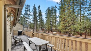 A wooden deck with a picnic table and benches, surrounded by a wooden railing, overlooking a forested area.