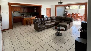 Un amplio salón con un sofá seccional en forma de L, una cocina con armarios de madera y un comedor con mesa y sillas.