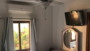 Un dormitorio con dos camas, ventilador de techo, televisor, cómoda con cajones y ventana con cortinas.