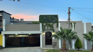 Una casa moderna de dos pisos con garaje, entrada protegida por una reja y un pequeño jardín con palmeras.