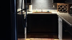 A kitchen with dark cabinets, a black refrigerator, a tiled backsplash, and a wooden wine rack. - Mountain Modern Condo (Cody)